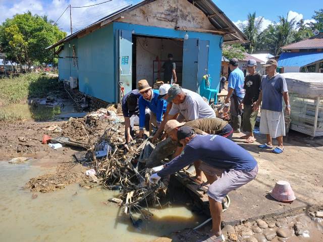 Aparat Desa Tutuyan mengangkut sampah dan lumpur dari area terdampak banjir. Gotong royong dilakukan bersama warga.
