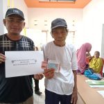 Sangadi Tutuyan Mikdad Modeong mengenakan kaos hitam bergaris putih saat menyerahkan bantuan BLT kepada Keluarga Penerima Manfaat.
