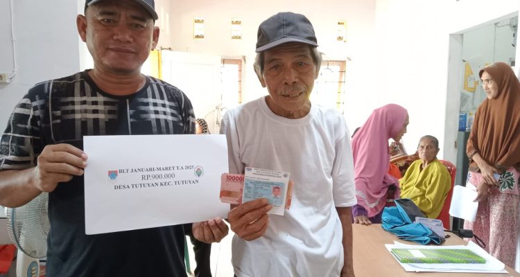 Sangadi Tutuyan Mikdad Modeong mengenakan kaos hitam bergaris putih saat menyerahkan bantuan BLT kepada Keluarga Penerima Manfaat.