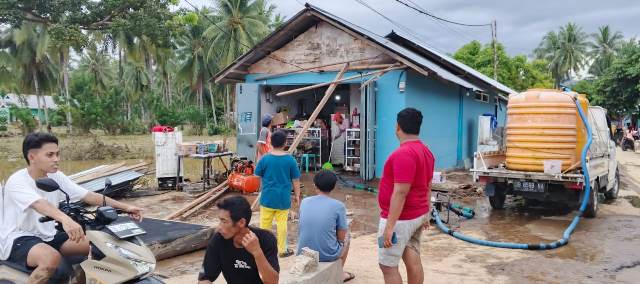 Warga berkumpul di depan rumah yang terdampak banjir bandang di Desa Togid, Kecamatan Tutuyan, Boltim. Sejumlah alat rumah tangga tampak dikeluarkan untuk dibersihkan dari lumpur.
