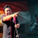 Ramdan Buhang berdiri di depan latar bendera Merah Putih peringatan 80 tahun kemerdekaan. Sebuah ironi, ketika simbol kebanggaan bangsa berkibar megah, pelayanan kesehatan di dalam negeri justru membuat rakyat mencari harapan di negeri orang.