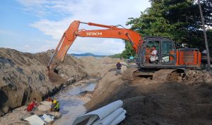 Pekerja proyek bersama alat berat ekskavator menata batu bolder pada pembangunan pengaman pantai di kawasan Batu Pinagut, Desa Boroko Timur, Kecamatan Kaidipang, Kabupaten Bolaang Mongondow Utara. Proyek ini telah mencapai progres fisik 50,05 persen dan berjalan tanpa kendala. (Foto: dok. binadow.com)