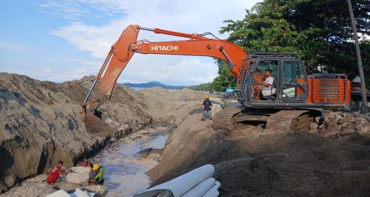 Pekerja proyek bersama alat berat ekskavator menata batu bolder pada pembangunan pengaman pantai di kawasan Batu Pinagut, Desa Boroko Timur, Kecamatan Kaidipang, Kabupaten Bolaang Mongondow Utara. Proyek ini telah mencapai progres fisik 50,05 persen dan berjalan tanpa kendala. (Foto: dok. binadow.com)