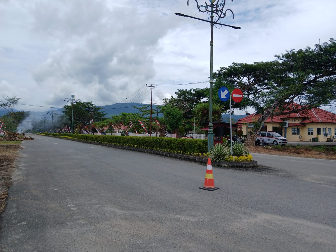 Kondisi ruas jalan di kompleks perkantoran Pemerintah Kabupaten Bolaang Mongondow Utara, Rabu, (6/8/2025), setelah batang dan ranting pohon hasil penebangan dibersihkan. Sebelumnya, tumpukan kayu sempat menghalangi akses jalan di depan sejumlah kantor OPD. Tampak asap sisa pembakaran limbah kayu masih mengepul di kejauhan.