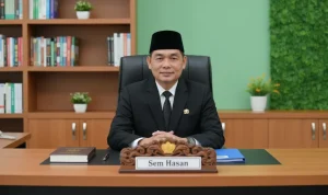 Potret resmi Sem Hasan, Anggota DPRD Boltara, duduk di meja kerjanya mengenakan jas hitam dan peci.