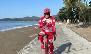 Amin Lasena di atas sepeda di tepi Pantai Batu Pinagut, satu kaki berjinjit, satu tangan