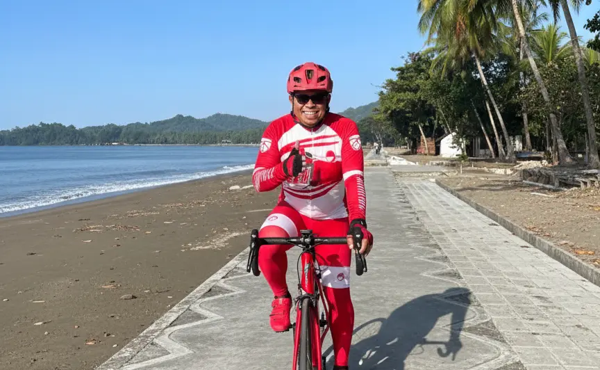 Amin Lasena di atas sepeda di tepi Pantai Batu Pinagut, satu kaki berjinjit, satu tangan