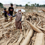 Warga berjalan melewati hamparan kayu gelondongan dan puing banjir bandang di kawasan terdampak Aceh.
