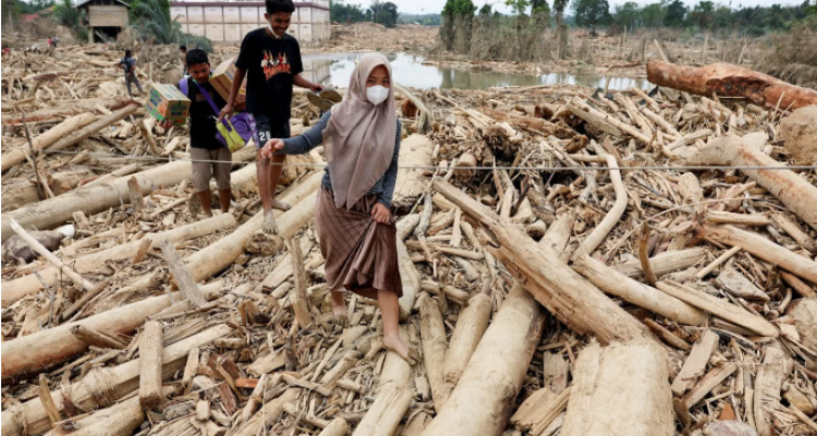 Warga berjalan melewati hamparan kayu gelondongan dan puing banjir bandang di kawasan terdampak Aceh.