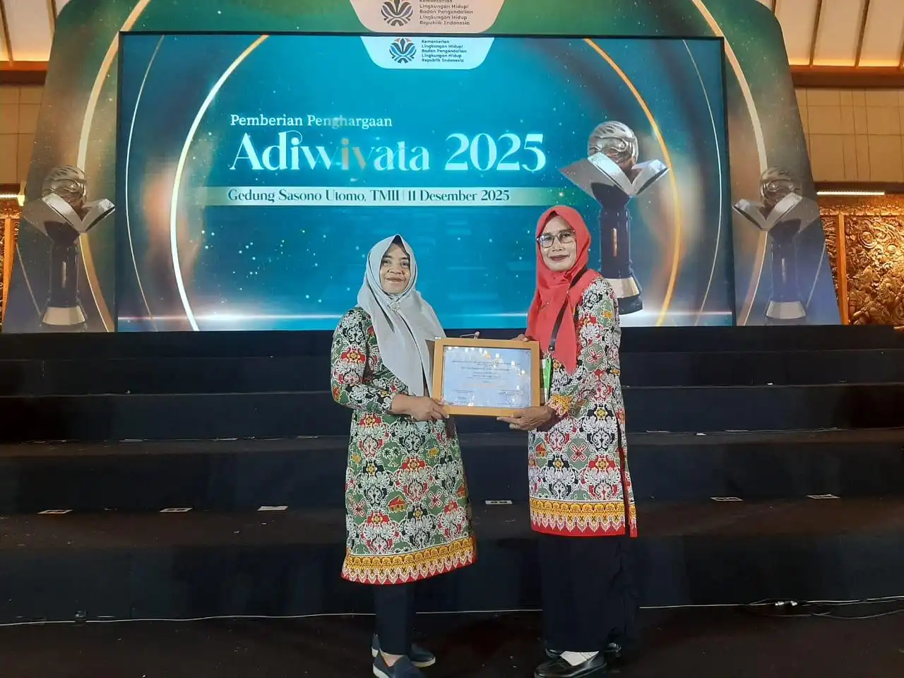 Dua perwakilan SDN 11 Pinogaluman berpose di panggung usai menerima Penghargaan Adiwiyata Nasional 2025 di Gedung Sasono Utomo, TMII Jakarta.