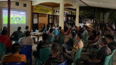 Warga bersama personel Polsek Pinogaluman mengikuti nonton bareng pertandingan FIFA World Cup 2026 di halaman Mako Polsek Pinogaluman, Selasa dini hari, (23/6/2026).