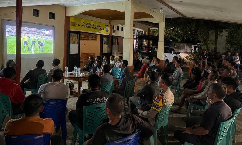 Warga bersama personel Polsek Pinogaluman mengikuti nonton bareng pertandingan FIFA World Cup 2026 di halaman Mako Polsek Pinogaluman, Selasa dini hari, (23/6/2026).