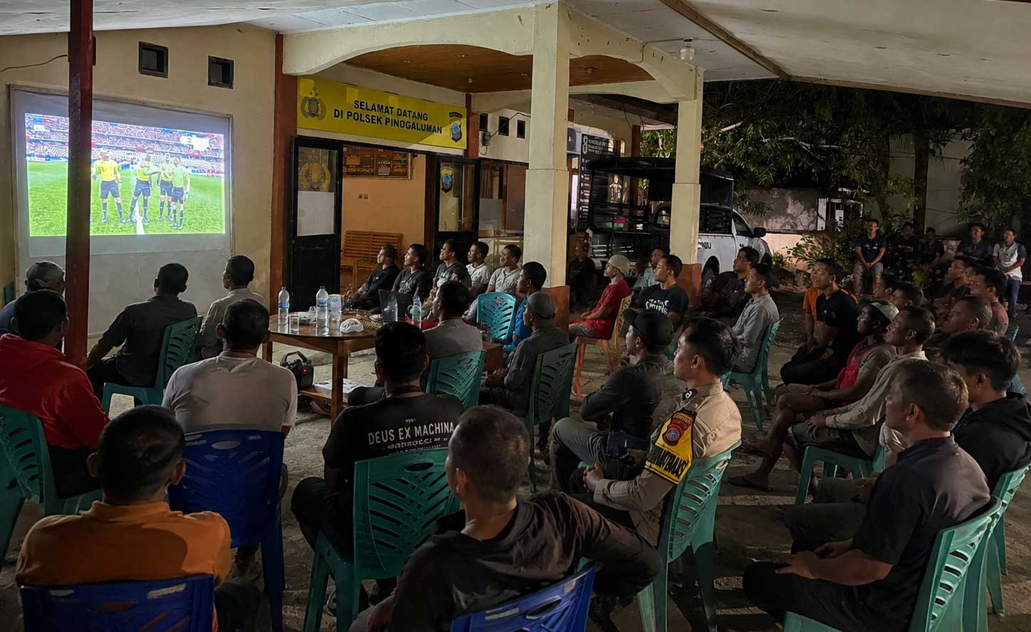 Warga bersama personel Polsek Pinogaluman mengikuti nonton bareng pertandingan FIFA World Cup 2026 di halaman Mako Polsek Pinogaluman, Selasa dini hari, (23/6/2026).